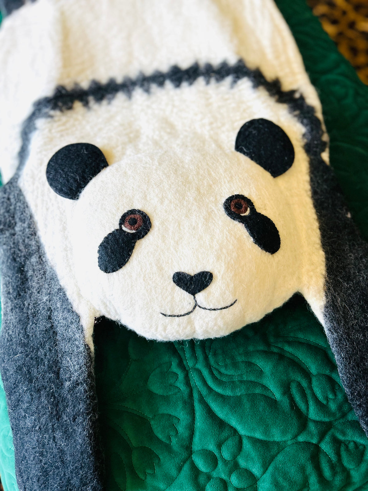 Close-up of Ping the Panda felt rug showing its white face, black ears and panda markings on a green background