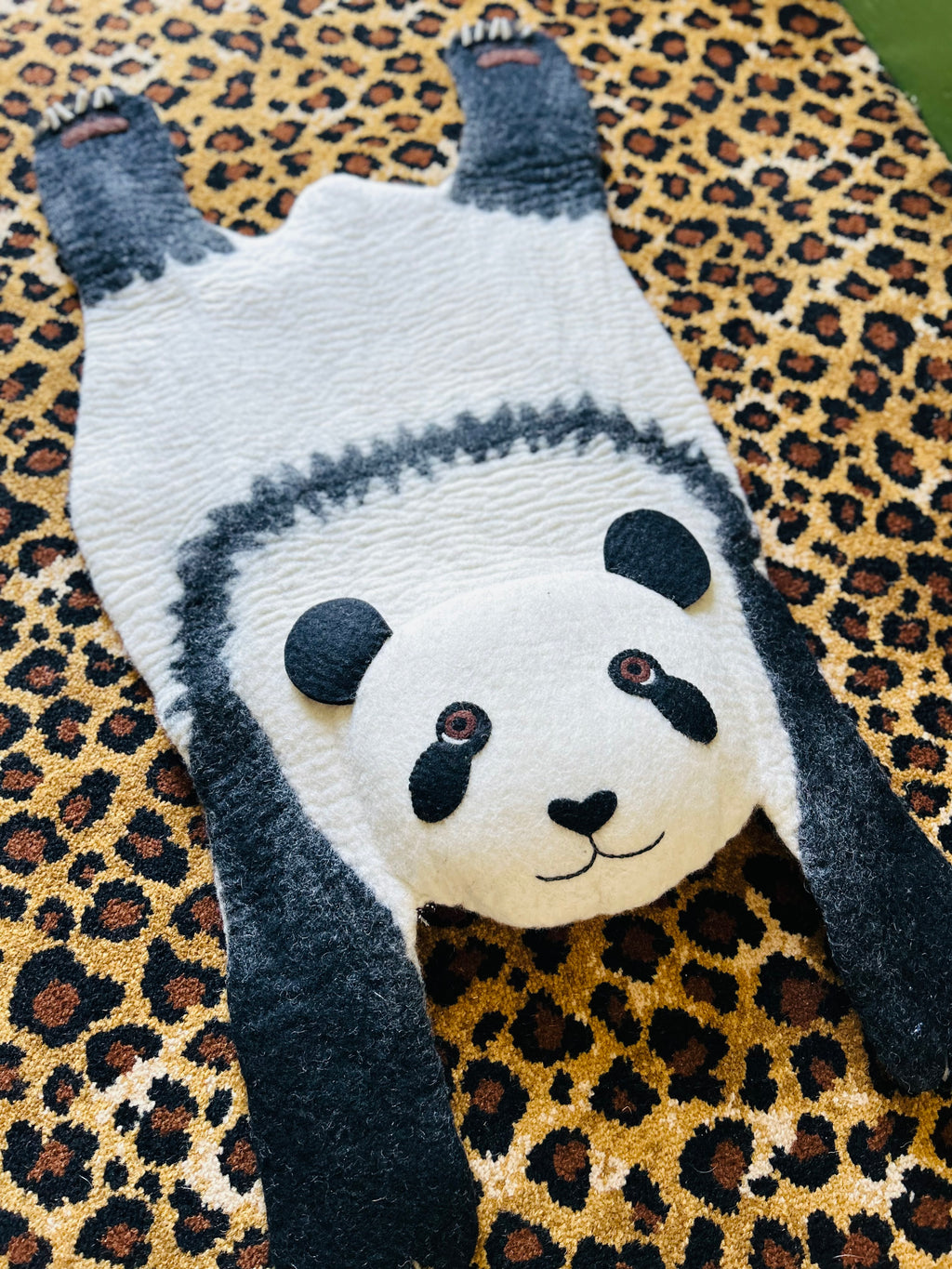 Ping the Panda felt rug with a white face and black ears, legs and panda markings on a leopard-print rug