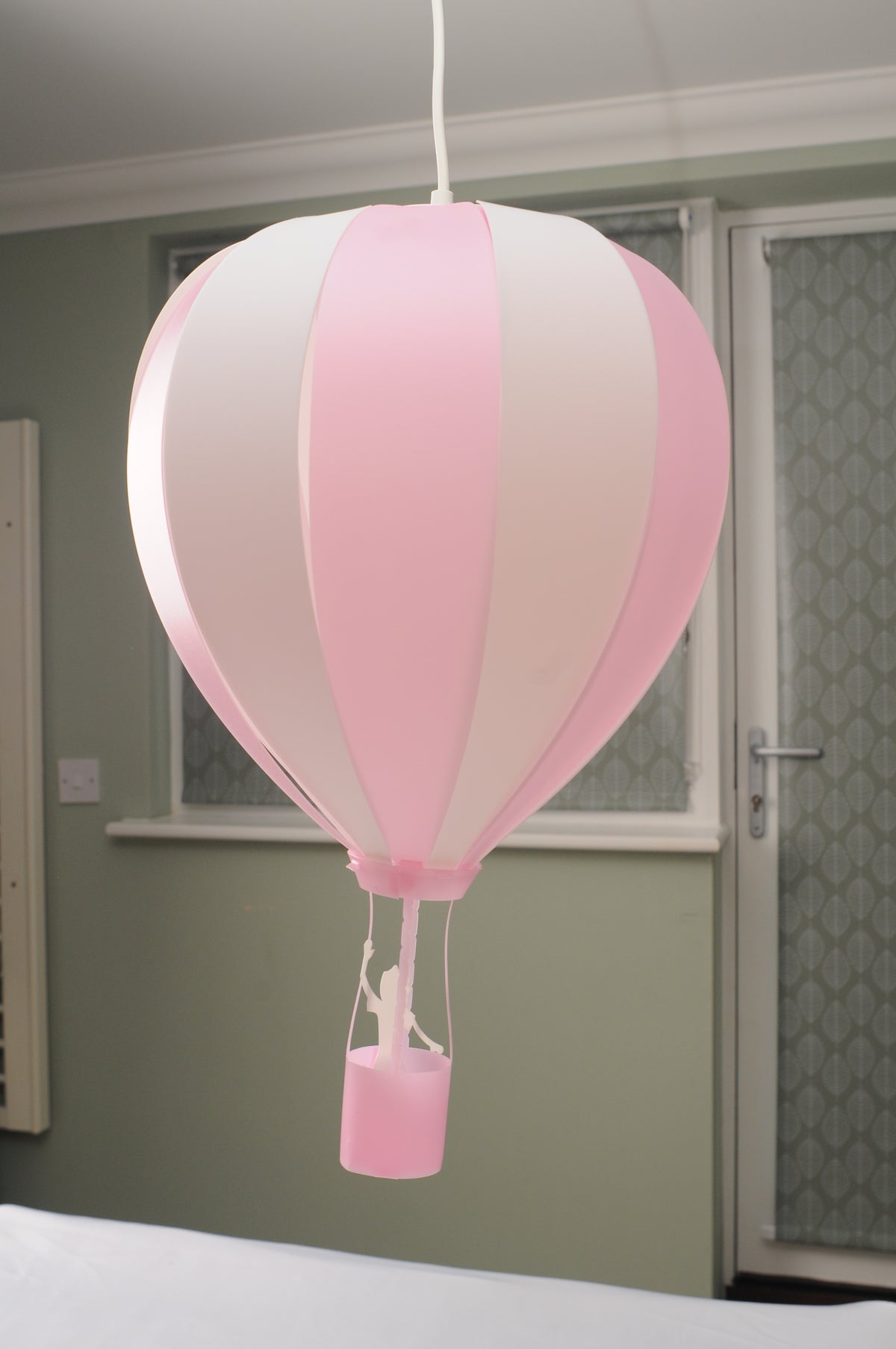 Pink and white striped hot air balloon pendant light hanging in a child’s bedroom above a bed
