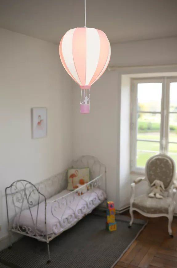 Pink and white striped hot air balloon pendant light hanging in a child’s room above a small bed beside a window