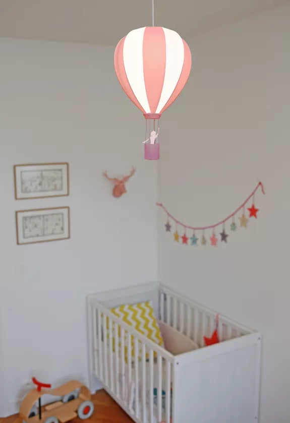 Pink and white striped hot air balloon pendant light hanging above a white cot in a colourful nursery