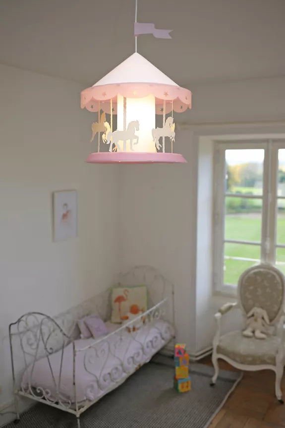 Pink merry-go-round pendant light glowing above a child’s cot in a nursery room