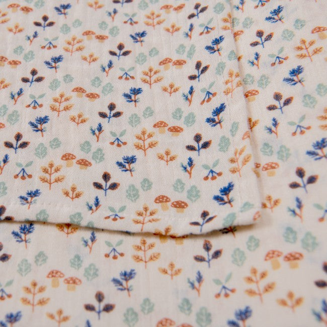 Close-up of the Pomme des Bois changing mat showing its cream fabric and delicate blue, sage green, ochre and brown botanical print
