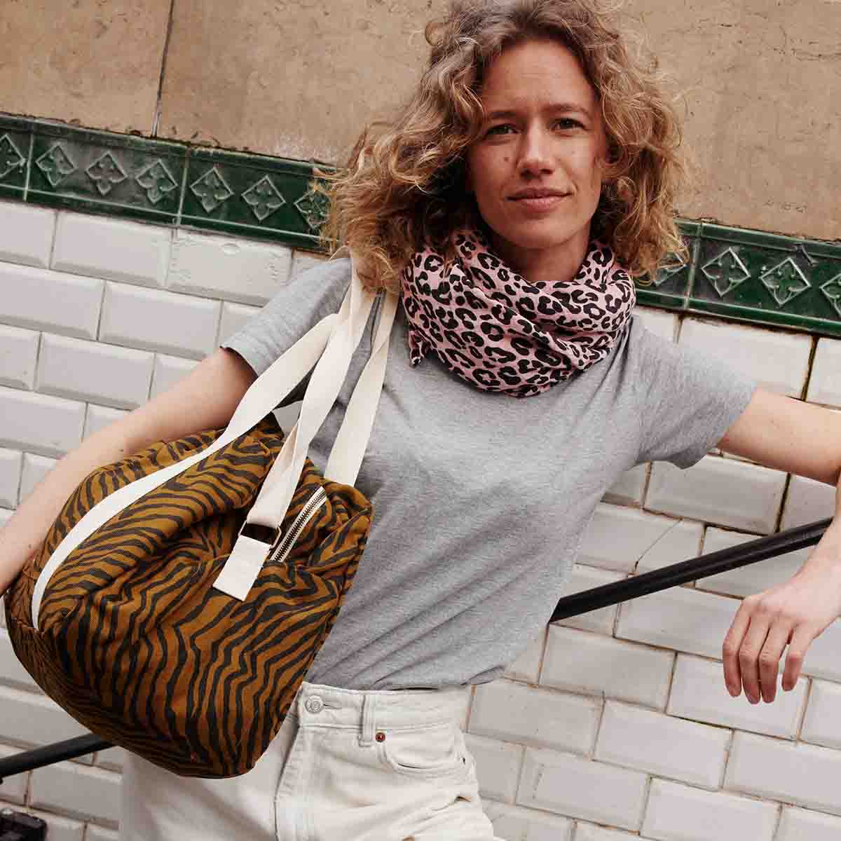Woman posing with the Tapenade Zebra Raphael weekend bag over her shoulder, highlighting its spacious design, bold zebra print and cream straps.