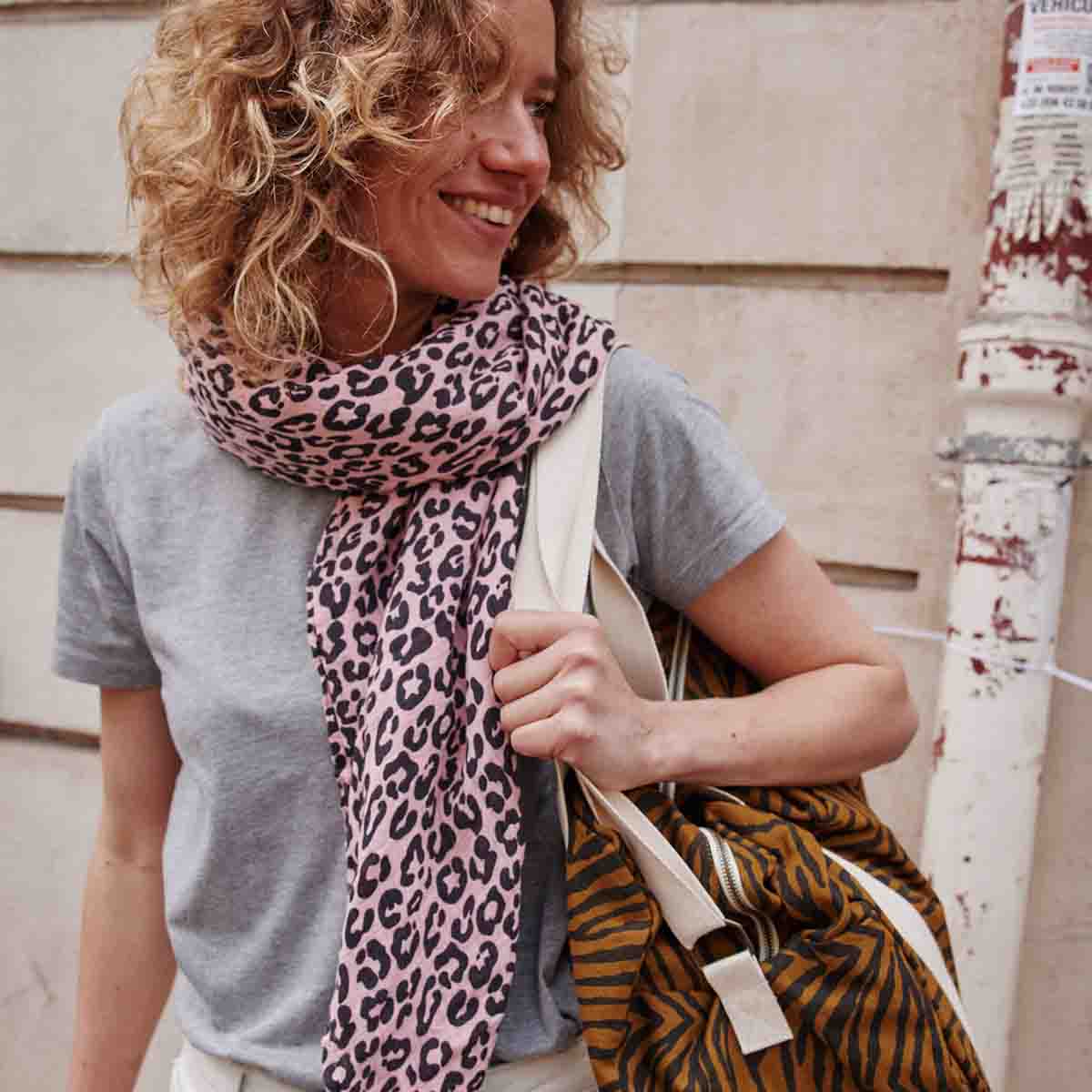 Woman wearing a grey top and pink leopard print scarf while carrying the Tapenade Zebra Raphael weekend bag over her shoulder.