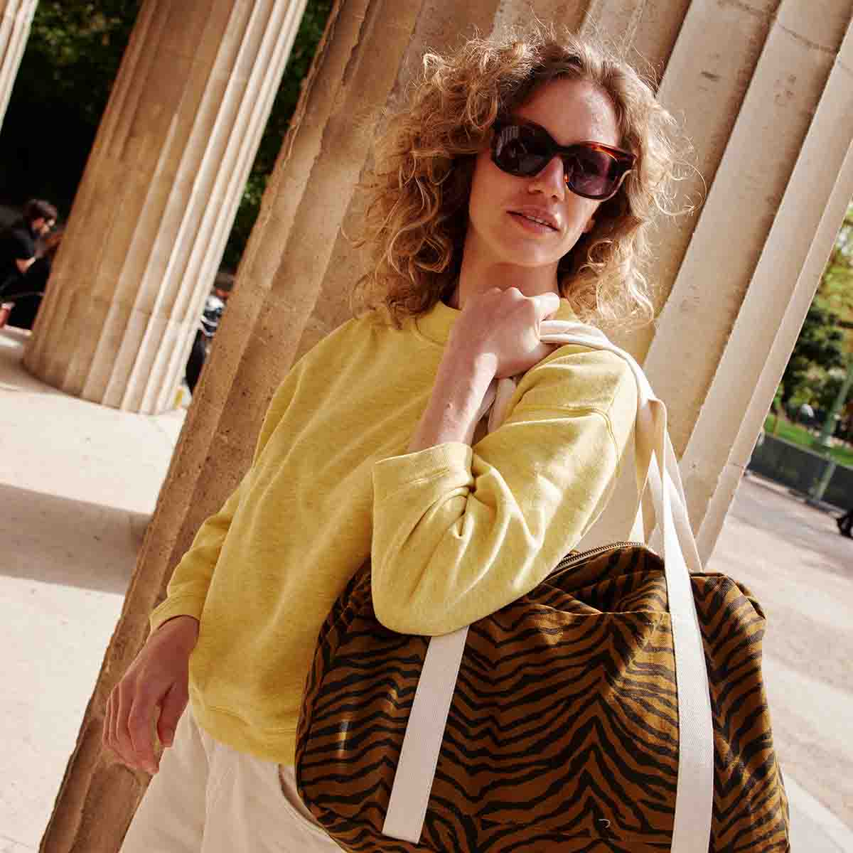 Woman carrying the Raphael weekend bag in Tapenade Zebra print over her shoulder, showcasing its brown and black pattern and cream straps.