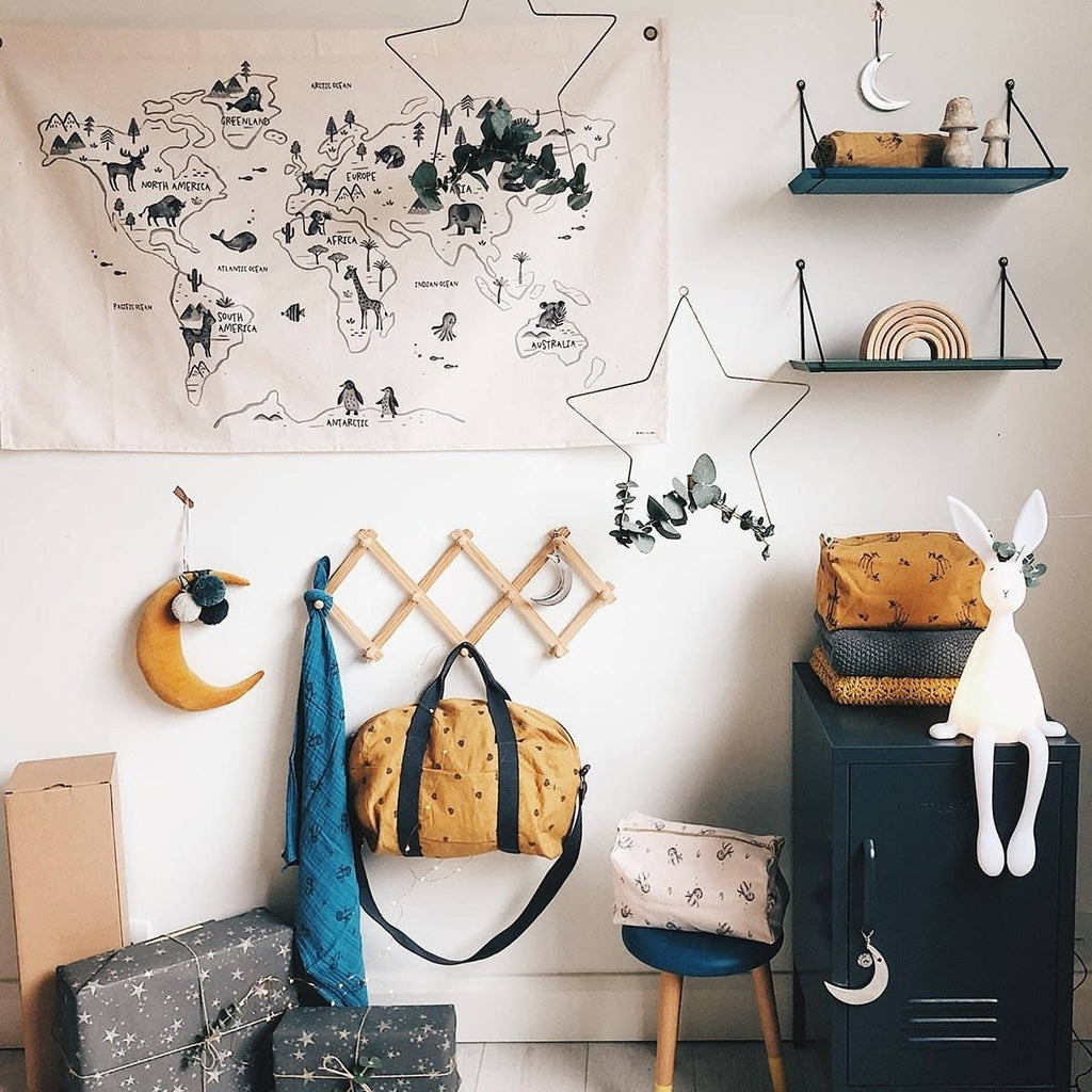 White Joseph Bunny night light displayed on a dark bedside cabinet in a nursery, surrounded by wall shelves, a world map tapestry, hanging decorations and storage bags.