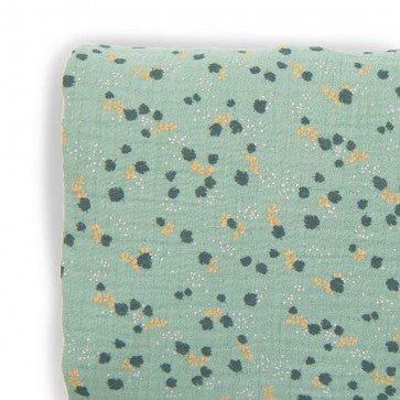 Close-up of sage green cotton muslin cot sheet showing its delicate botanical pattern