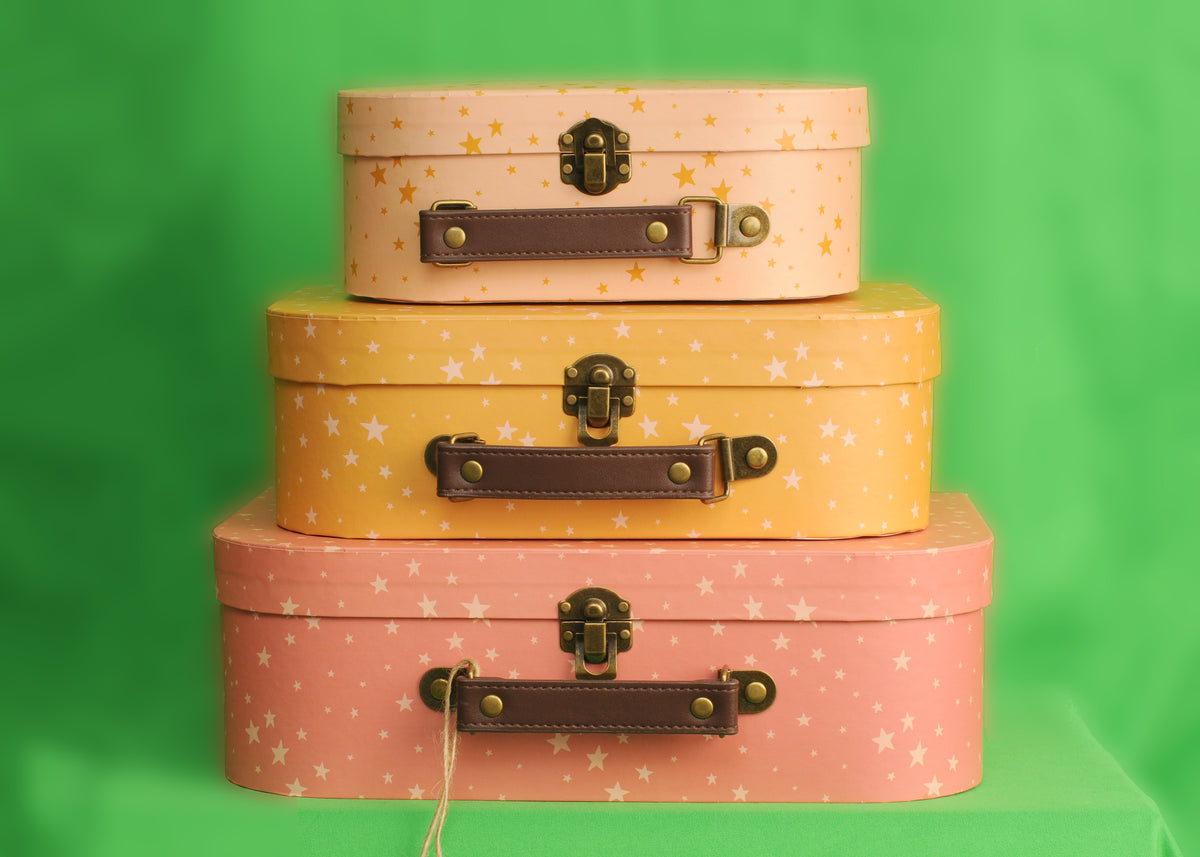 Three pink and orange star-patterned decorative suitcases stacked together against a green background