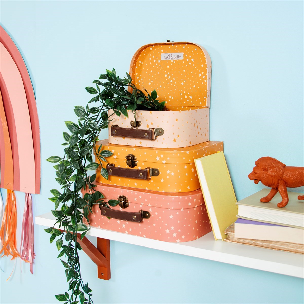 Set of three pink and orange star-patterned decorative suitcases stacked on a shelf with books and plants