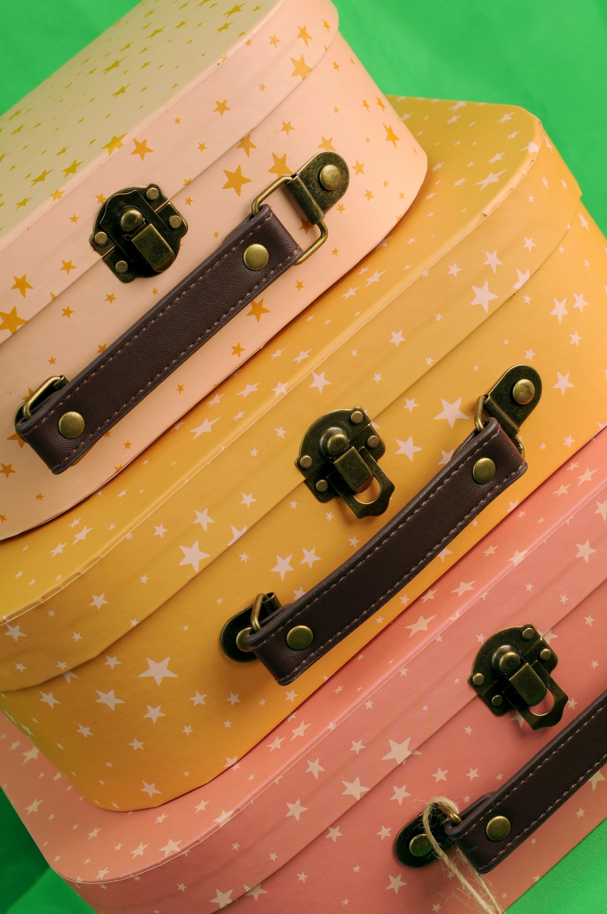 Close-up of three pink and orange decorative suitcases with star patterns, brown handles and brass-coloured clasps
