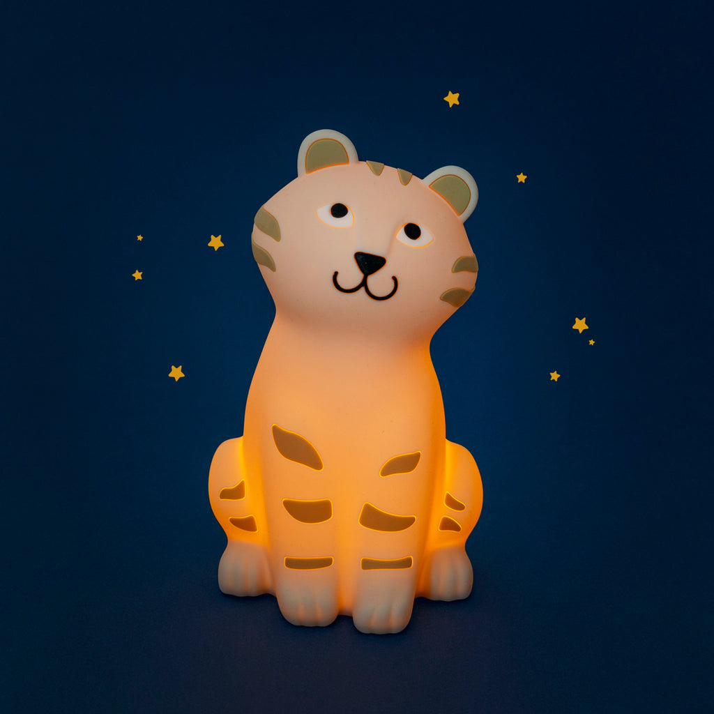 Moulin Roty La Forêt Mawa tiger night light glowing warm orange, with golden-yellow stripes and a friendly face, against a dark blue background with small stars.