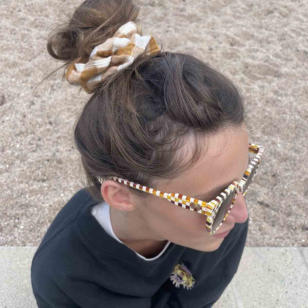 Woman wearing the Vichy Caramel gingham scrunchie in a high bun, paired with checked sunglasses for a coordinated casual look.
