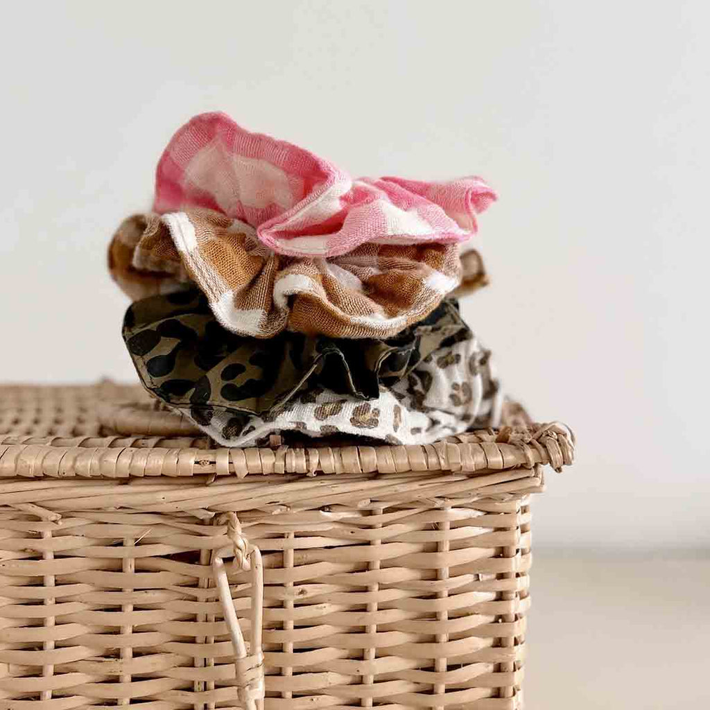 Caramel and cream gingham scrunchie stacked with pink gingham and animal-print scrunchies on a woven basket.