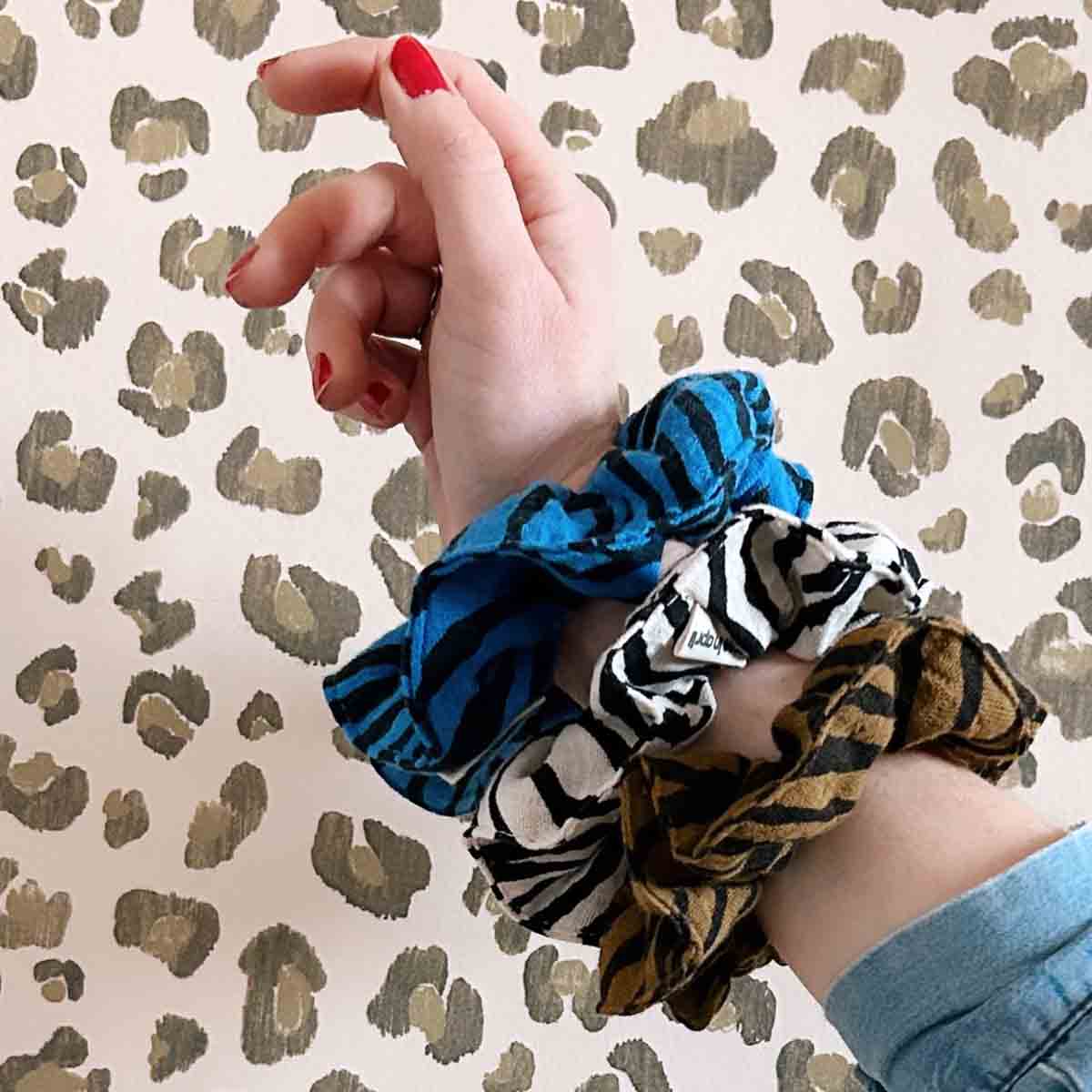 Three patterned scrunchies in Greek blue zebra, black and white zebra, and brown animal print worn together on a wrist.